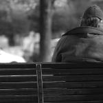 Black and white photo of a person sitting on a bench with their back to us