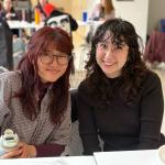 Two students lean together and smile in Noble Commons