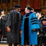 David Miller and Marji Edguer smile at each other and hold hands on stage at commencement 2025