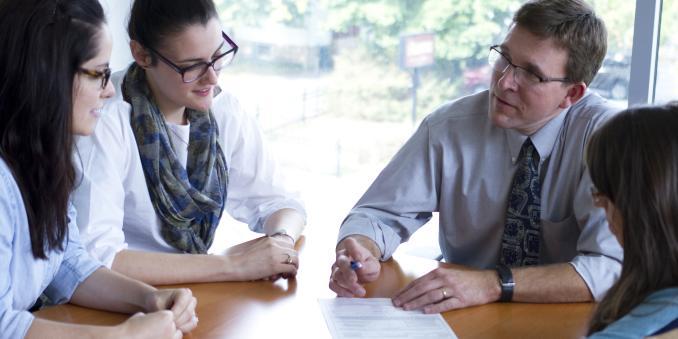 Faculty sitting and talking with three students at table