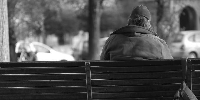 Black and white photo of a person sitting on a bench with their back to us