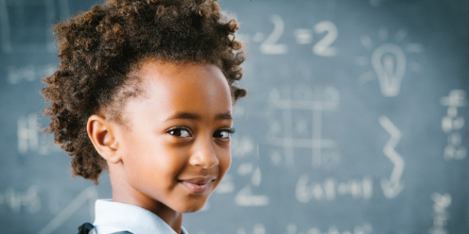 Girl looks back and smiles in front of a chalkboard with math problems on it