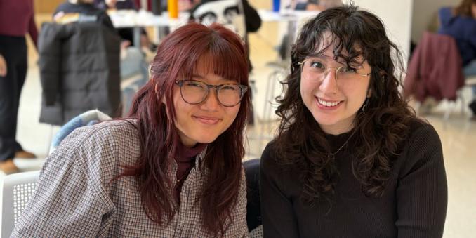 Two students lean together and smile in Noble Commons