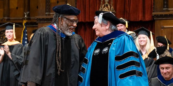 David Miller and Marji Edguer smile at each other and hold hands on stage at commencement 2025