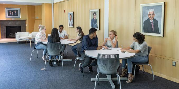 7 students sit at tables in Mandel Center and discuss things