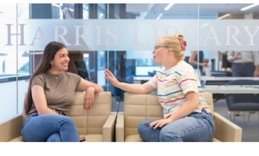 Two female students talking in front of the Harris Library lettering