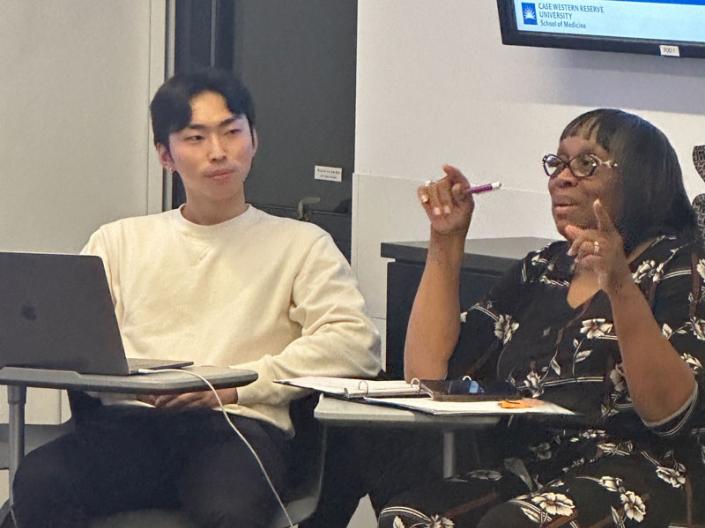 One student looks on as another talks to the class