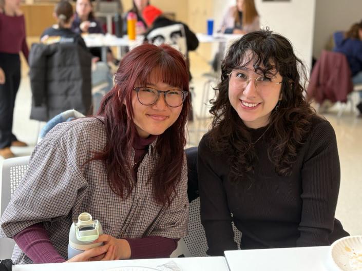 Two students lean together and smile in Noble Commons