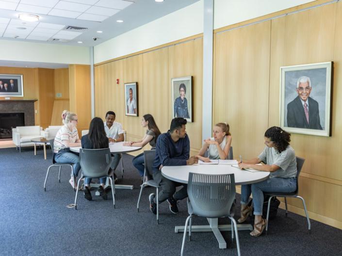 7 students sit at tables in Mandel Center and discuss things