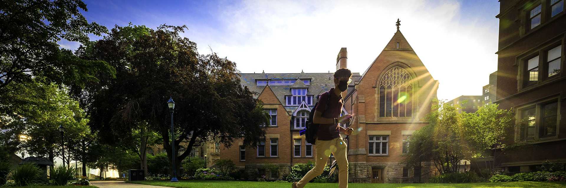 Photo of a Case Western Reserve University student walking across Mather Quad with prominent sun rays shining down
