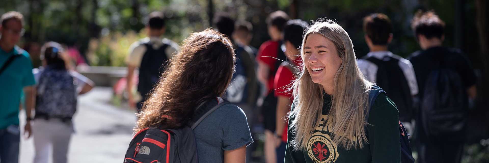 Photo of two Case Western Reserve University students talking outside, one facing the camera and smiling and the other with their back to the camera