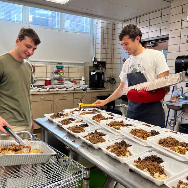 Two male students preparing dozens of boxes of food.