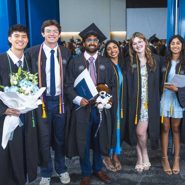 A group of six people posing in caps and gowns in Tinkham Veale University Center.