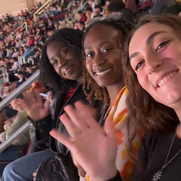 Three students waving at the camera in the stands at Rocket Arena.