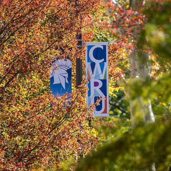 A banner reading “CWRU” hanging from a lamppost surrounded by colorful fall foliage.