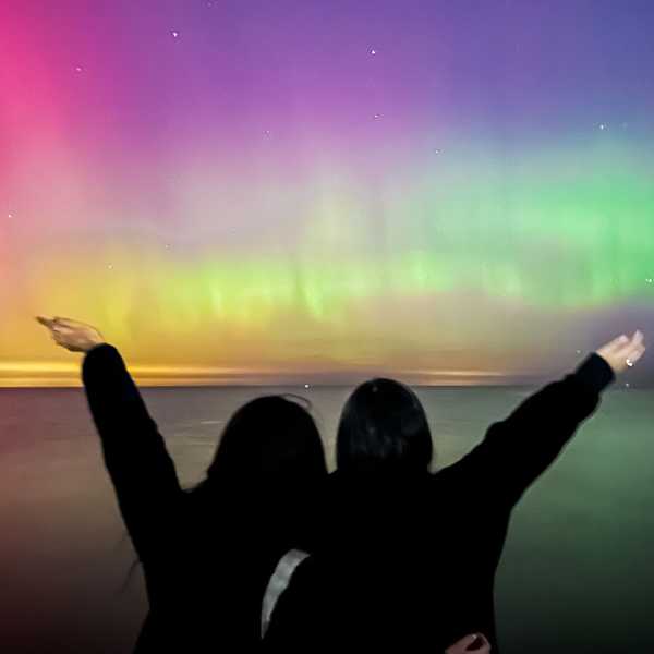 Two CWRU students pose with their arms raised watching the lights of the aurora borealis over Lake Erie.