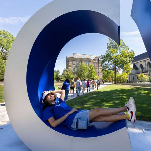 A student lounging in the letter “C” of the “CWRU” sign on campus.