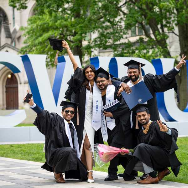 A group of five CWRU students posing with their arms in the air in front of a CWRU sign on campus.