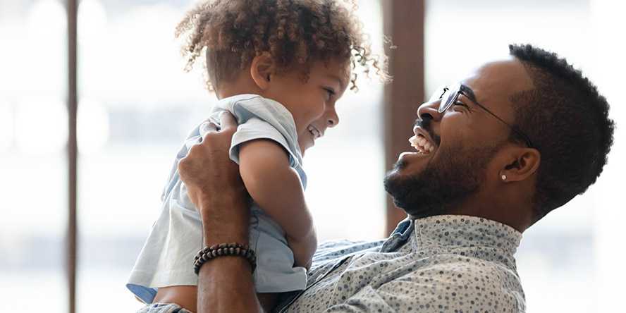 Photo of a man holding a young child at eye level, smiling