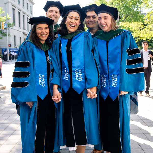 Five CWRU School of Medicine students pose for a photo in their academic regalia holding hands. 