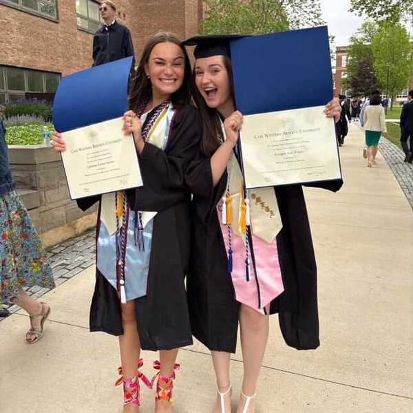 Two women posing in graduation gowns, holding their Case Western Reserve University diplomas.
