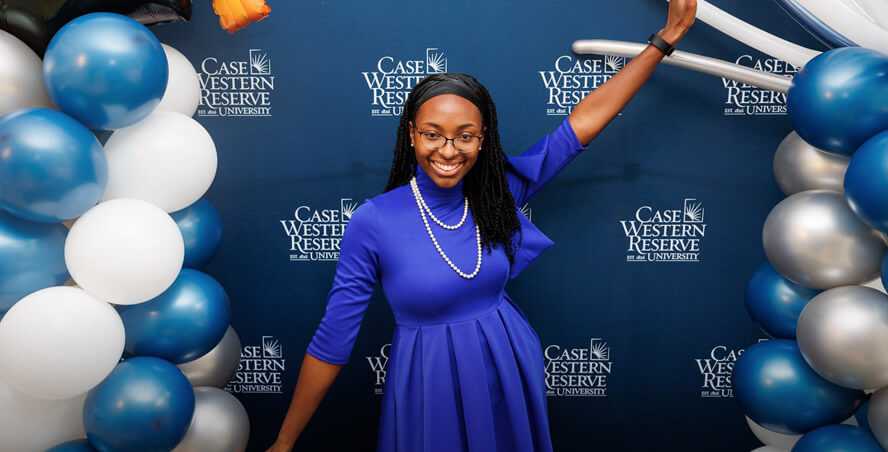 Photo of a Case Western Reserve University alum standing in front of a CWRU backdrop with balloons surrounding