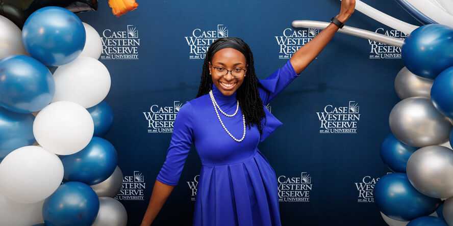 Photo of a Case Western Reserve University alum standing in front of a CWRU backdrop with balloons surrounding