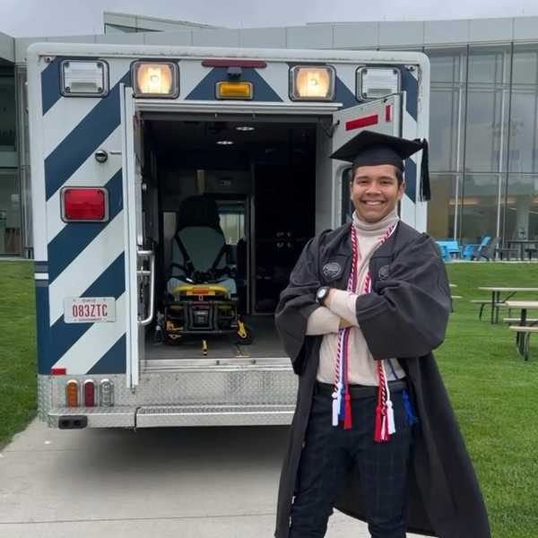Alex Flores posing behind the CWRU EMS ambulance in his undergraduate regalia.