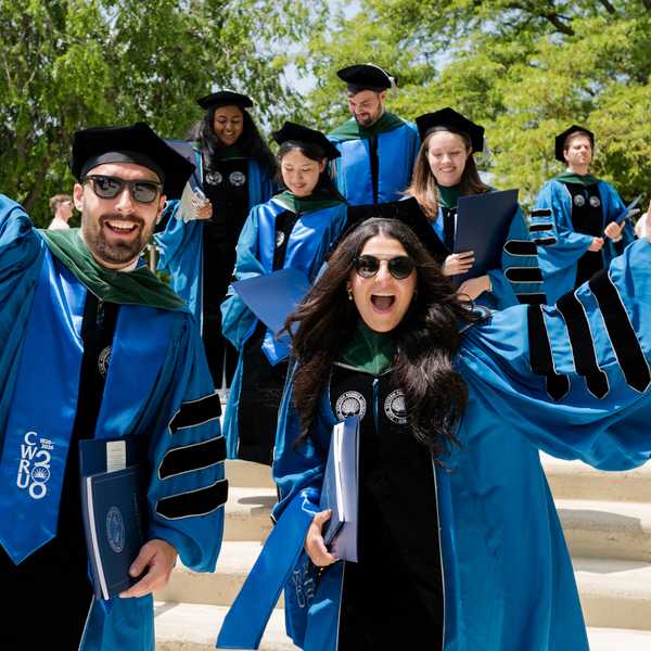 Two CWRU School of Medicine students waving to the camera with fellow graduates visible in the background.