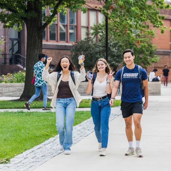 A group of three students smiling and posing while walking across campus.