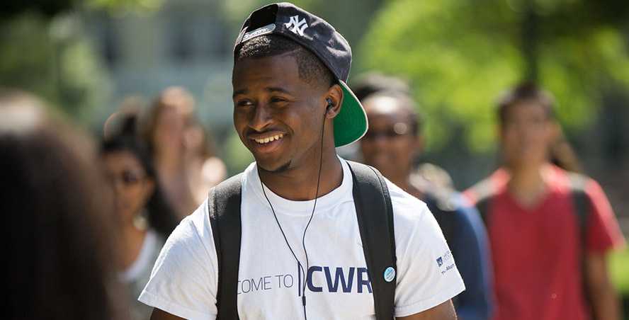 Photo of a Case Western Reserve University student wearing headphones, walking outdoors and smiling