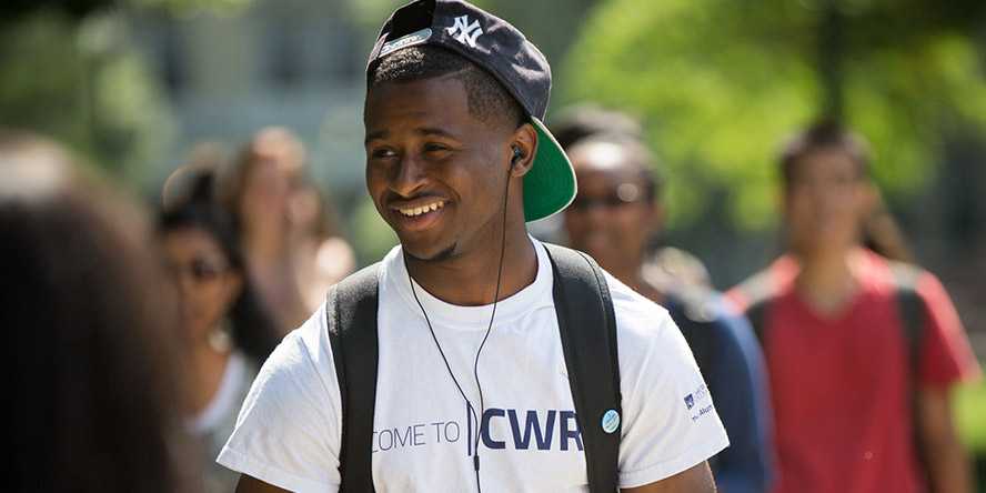 Photo of a Case Western Reserve University student wearing headphones, walking outdoors and smiling