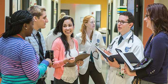 Photo of a group of Case Western Reserve University students, some in plain clothes and others in white coats, talking in a hospital setting