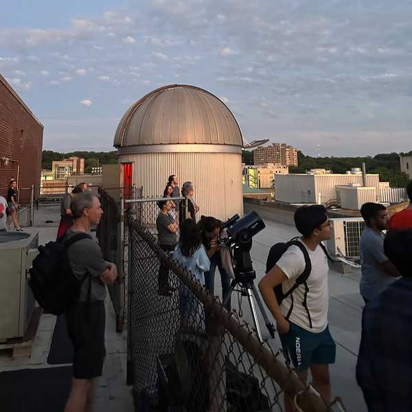 Members of the CWRU community on a roof, looking at the sky near the AW Smith Rooftop Telescope.