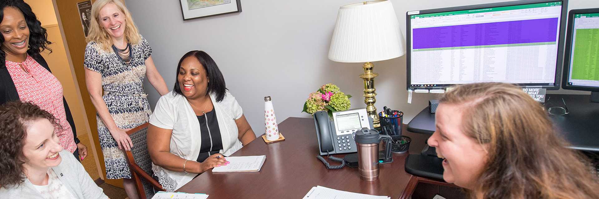 Photo of a group of Case Western Reserve University staff members talking and smiling around a desk