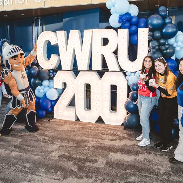 A group of five people and mascot Spartie pose in front of light-up letters that spell, “CWRU 200.”