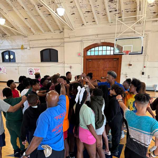 Children and camp instructors put their hands together in a team-building huddle inside Adelbert Gymnasium.