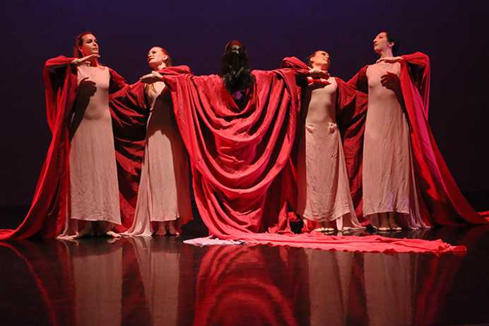 Photo of a performance at Case Western Reserve University, with students wearing long dresses and red robes