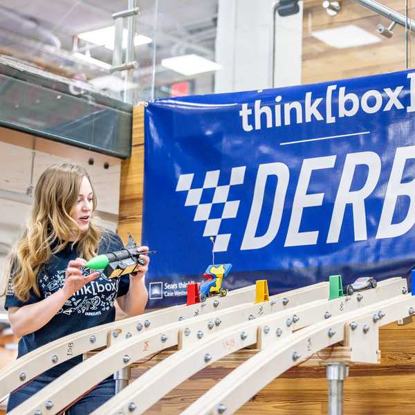 A woman placing a derby car on a track inside think[box] on campus.