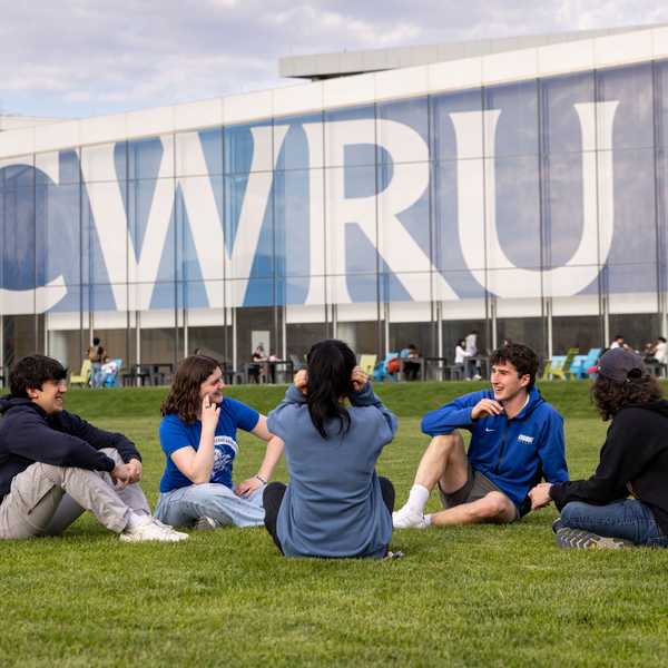 Five students sit in front of large “CWRU” signage on Freiberger Field.