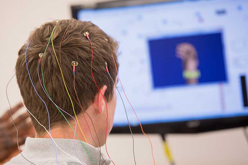 Photo of the back of a Case Western Reserve University student’s head with electrodes attached and a TV screen in background