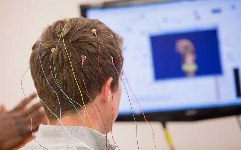 Photo of the back of a Case Western Reserve University student’s head with electrodes attached and a TV screen in background
