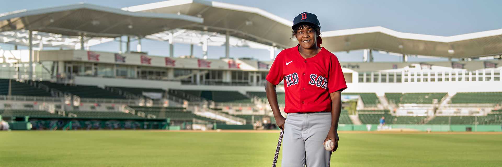 Photo of Case Western Reserve University alumna and MLB coach Bianca Smith stands in Boston Red Sox stadium holding a bat and baseball