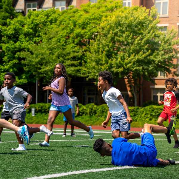 Participants in the National Youth Sports Program take part in a game of football at DiSanto Stadium on a sunny day.