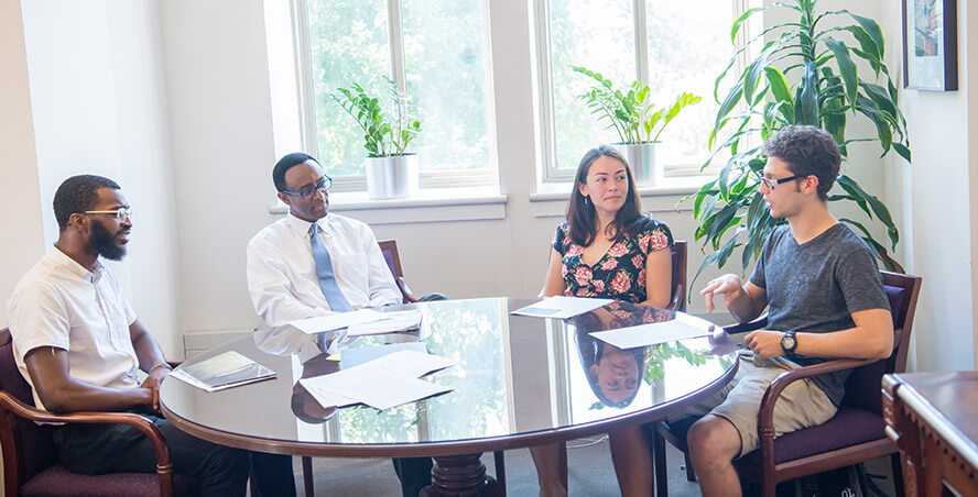 Photo of Case Western Reserve University Provost Ben Vinson III meeting with three students around a table in his office