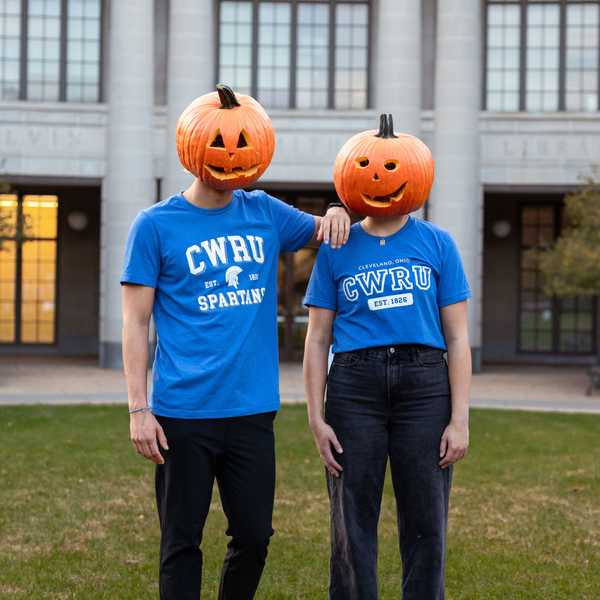 Two students posing with Jack-o-lanterns on their heads while wearing two different blue CWRU shirts.