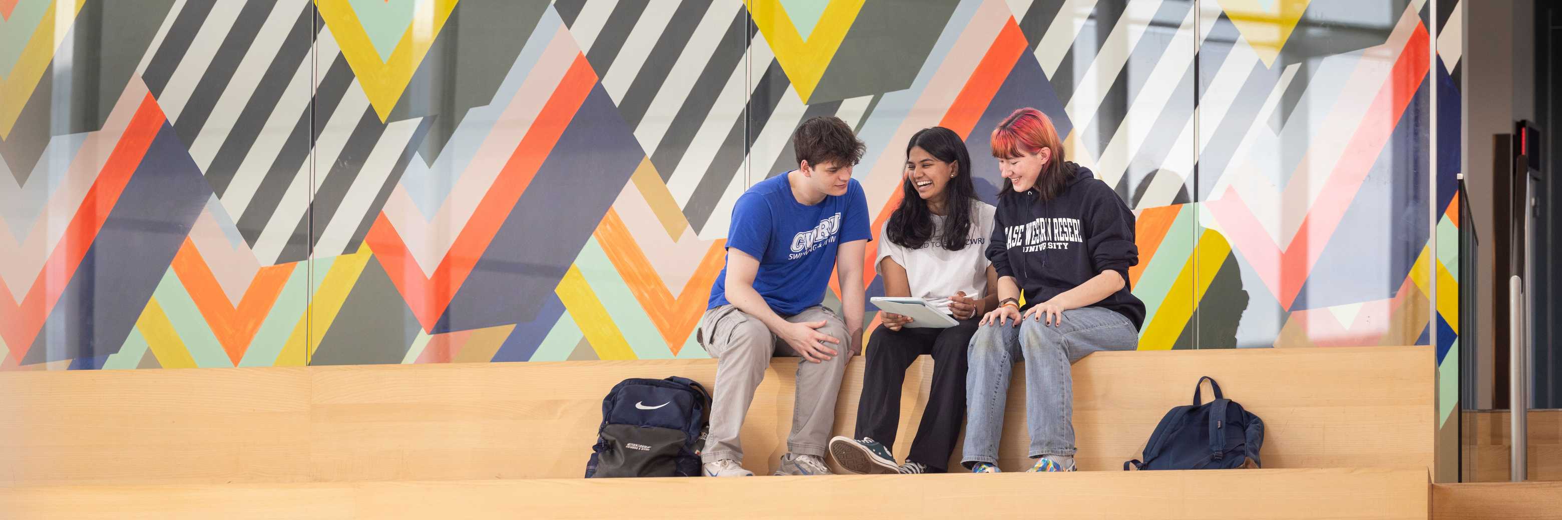 Three students study together beneath the colorful mural in the Tinkham Veale University Center