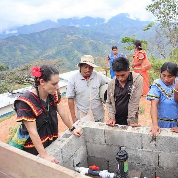 A group of people stand around a concrete structure housing a water pump system on a mountain in remote Panama.