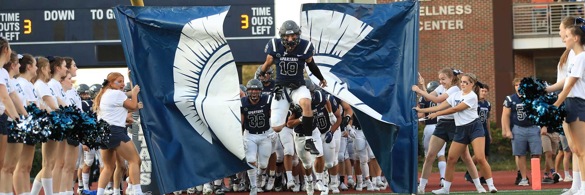 Photo of the Case Western Reserve University football team entering the field, with a player breaking through a banner that cheerleaders hold
