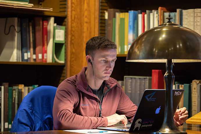 Photo of a Case Western Reserve University School of Law student looking at a computer in a library, wearing headphones